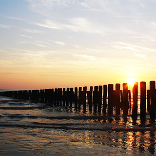 Zee De zon gaat achter de zee, gezien van achter een paalhoofd